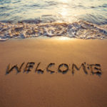 Sea shore sunset scene with the word "Welcome" written in the sand